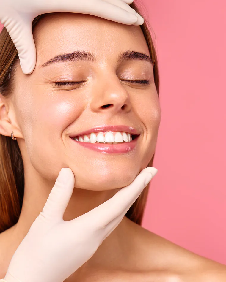 A smiling client with soft, refined lips, framed by a practitioner's gloved hands.
