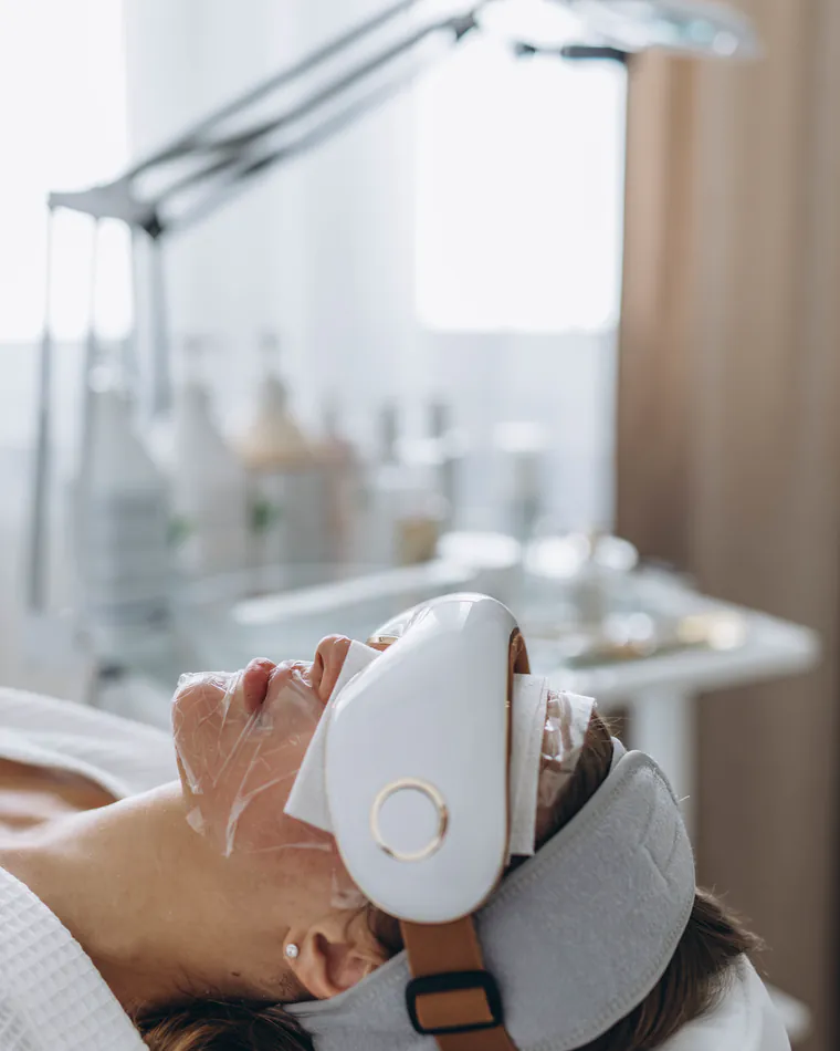 A client reclining under an LED light-therapy device in a calm treatment room.