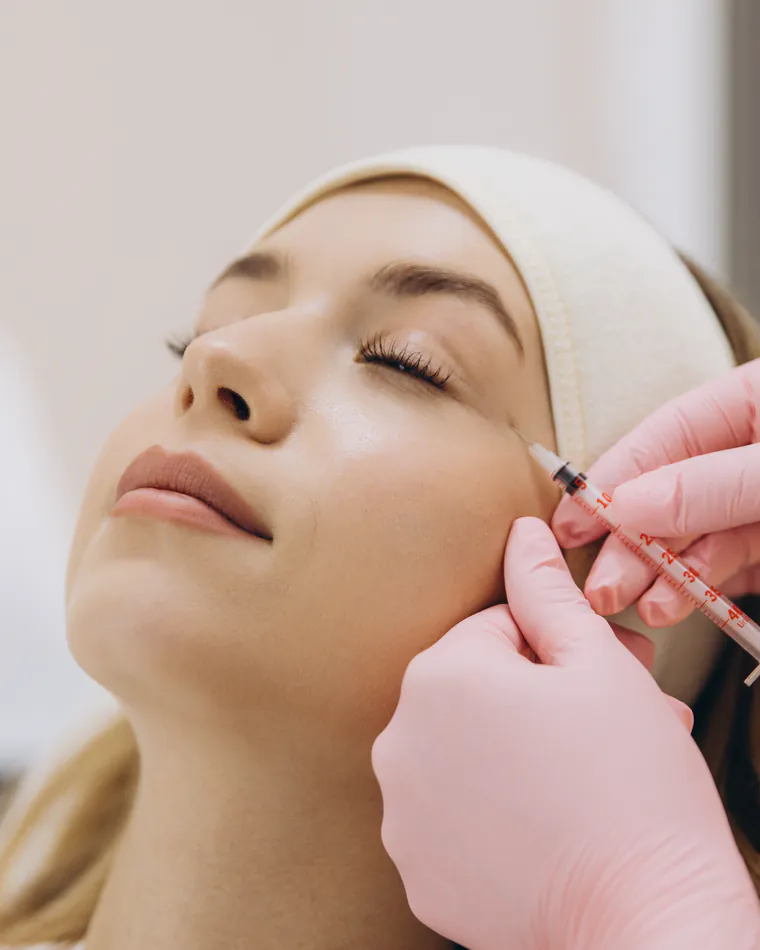 A gloved hand administering a fine injectable near the cheekbone of a relaxed client.