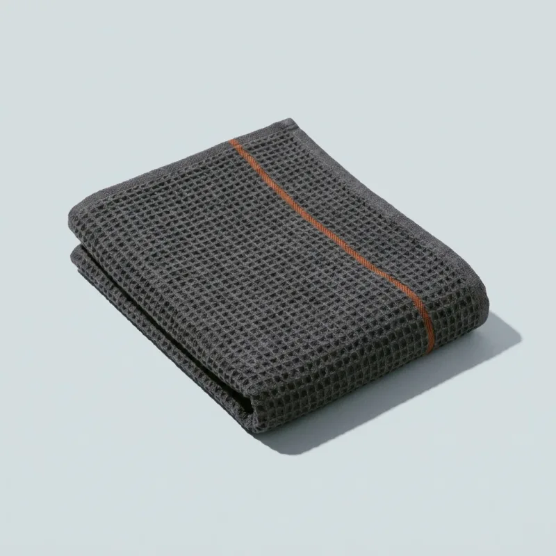 A folded charcoal waffle-weave sauna towel with an orange stripe