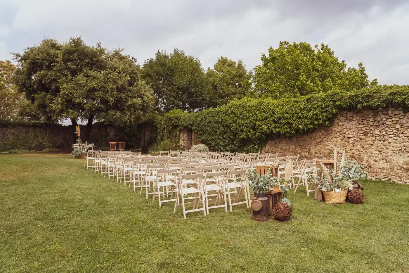Garden ceremony lawn framed by oaks, set with rows of chairs and a natural aisle.