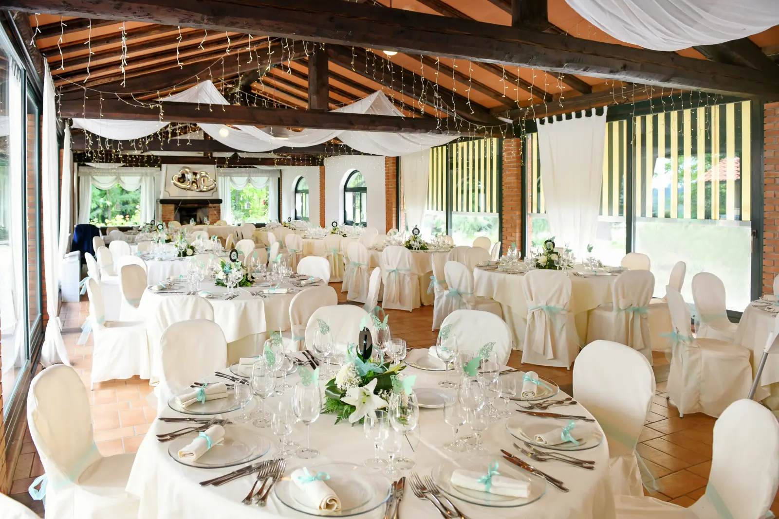Covered open-air reception pavilion set for dinner with string lighting.